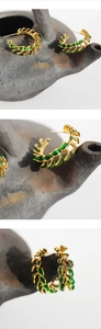 Detailed macro view of vintage gold metal earrings with green enamel leaves on grey pottery