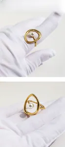 Détail d'une bague dorée abstraite ajourée ornée d'une perle blanche au centre