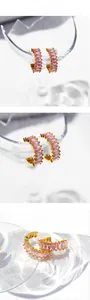 Detail shot of C-shaped gold earrings with rectangular pink zircons on glass