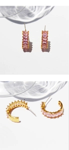 Detail of gold C-shaped earrings with rectangular pink zircon crystals on a bright background