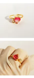 Detailed view of a gold plated heart ring with pink zircon and small round stone charm