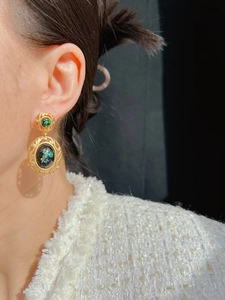Close-up of vintage gold oval earrings with hollow lace detailing and green resin inlay