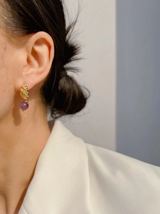 Detail of twisted gold stud earring featuring a vibrant purple agate bead drop on a model
