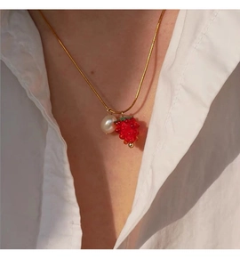 Detail of gold snake chain necklace featuring a white pearl and red berry pendant