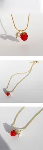 Detail of gold snake chain necklace featuring red raspberry and white pearl charms
