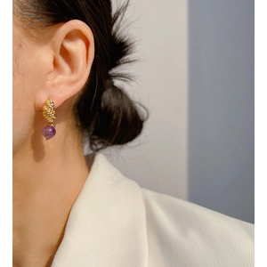 Elegant gold twisted hoop earrings featuring translucent purple agate beads worn by a model