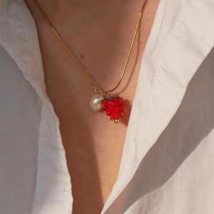 Gold snake chain necklace with pearl and red strawberry pendant on a white shirt