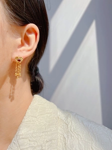Detail of vintage gold heart earring with red zircon gemstone and tassel chain fringes