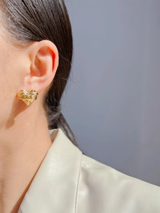 Close-up of golden heart earring with lava texture worn by a model in soft light
