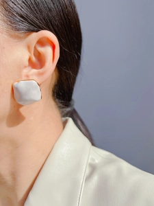 Close-up of model wearing geometric white enamel earrings with gold metal edges