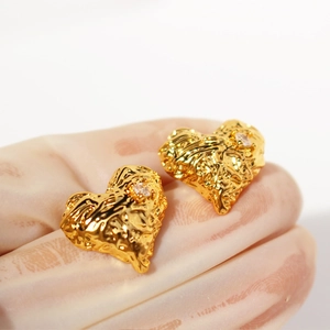 Golden heart earrings with molten lava texture and zircon accent on a gloved hand