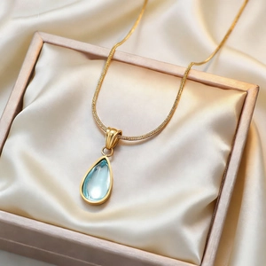 Elegant gold chain necklace with blue teardrop pendant on champagne silk satin