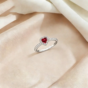 Detalle de anillo con gema roja de corazón y pavé sobre un fondo de seda rosa elegante
