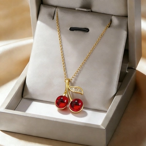 Titanium steel necklace featuring a red cherry pendant and sparkling leaf on white padding