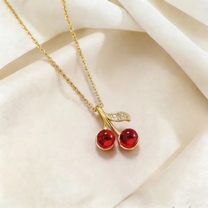 Titanium steel necklace with red cherry pendant and gold leaf on white silk background