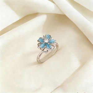 Rotating floral ring with blue cat eye stone petals and zircon center on silk background
