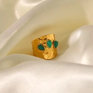 Detail eines goldenen Titanrings mit Hammerschlag-Textur und drei grünen Tropfensteinen