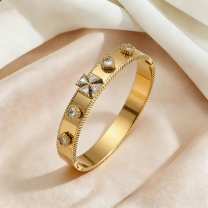 Gold titanium steel cuff bracelet with clover charms and zircons on satin background