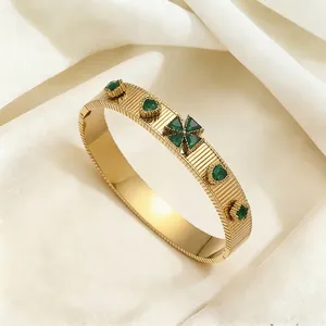 Golden striped titanium steel bangle featuring emerald green clover and heart gemstones