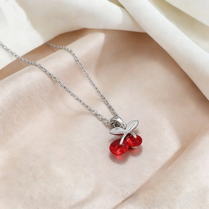 Elegant titanium steel necklace featuring red crystal cherry pendant on pink silk background