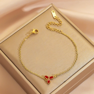 Elegant gold titanium steel bracelet with three-petal red clover charm on satin background