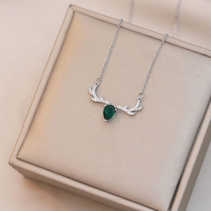 Macro detail of silver reindeer antler necklace featuring a green teardrop gemstone