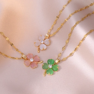 Three gold clover necklaces with white, pink, and green cat-eye stones on champagne silk