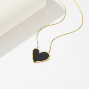Close-up of heart pendant with black onyx inlay and gold snake chain on white surface