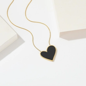 Detail of a golden snake chain necklace with a black enamel heart-shaped pendant