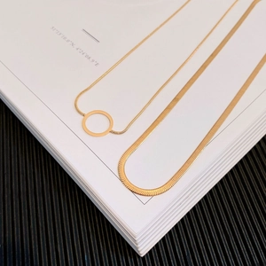 Detail of layered gold titanium steel necklaces with snake chain and circular pendant