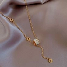 Detailed view of elegant gold Y-necklace with cylindrical pendant on satin fabric