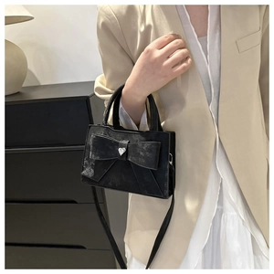 Détail du sac à main noir avec nœud et strass cœur sur une tenue de blazer beige