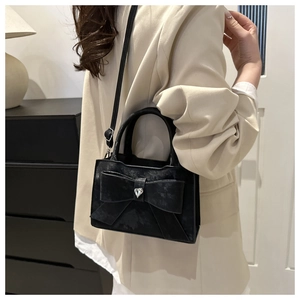 Détail du sac bandoulière noir avec nœud papillon et boucle cœur strass porté par un modèle