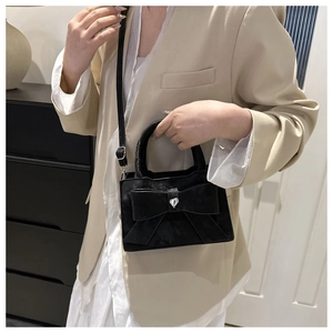 Détail d'un sac à main en velours noir avec nœud et strass en cœur porté par un modèle