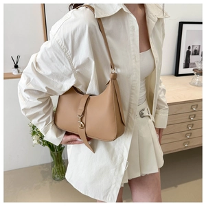 Detailed view of khaki hobo bag with gold buckle on model in warm home setting
