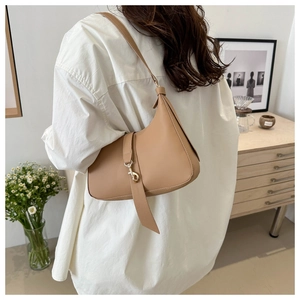 Model wearing a light brown leather crescent hobo bag with gold metal buckle detail