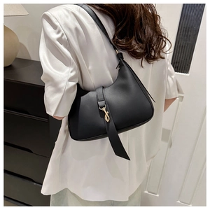 Close-up of black hobo bag with gold lobster clasp worn by model in white blazer