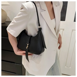 Detail of black leather hobo bag with gold metal hook closure on a white blazer outfit