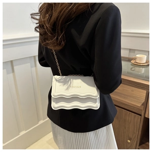 Detail showing white crossbody bag with scalloped edges and gold chain strap worn by model
