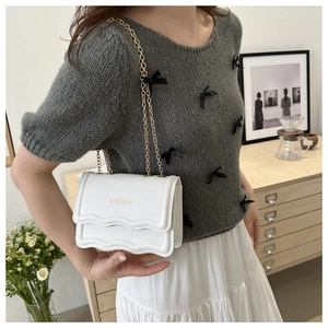 Detail of white litchi leather bag with wavy flap and golden chain strap