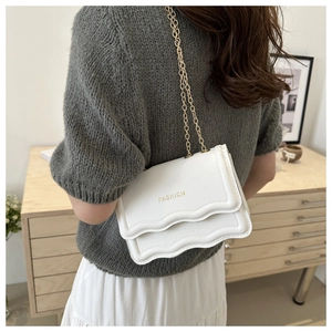 Détail d'un sac en cuir blanc à texture litchi avec chaîne dorée et rabat ondulé