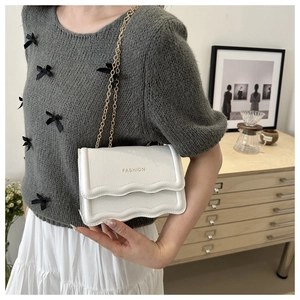 Détail d'un sac bandoulière blanc en cuir texturé avec bordure ondulée et chaîne dorée