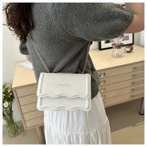 Close-up of white crossbody bag with scalloped edge detail and gold chain strap
