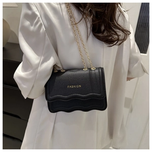 Détail d'un sac à main noir en cuir texturé avec chaîne dorée et base ondulée