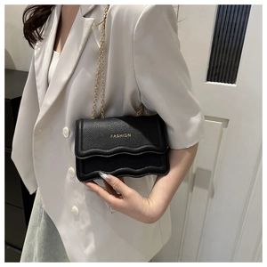 Détail du sac en cuir litchi noir avec rabat ondulé et chaîne dorée porté par un modèle