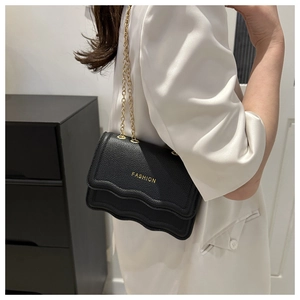 Détail du sac bandoulière noir à bords festonnés et chaîne dorée sur blazer blanc
