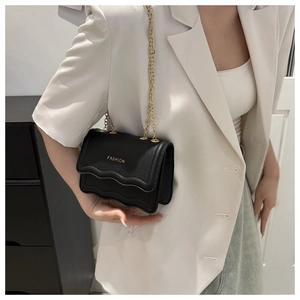 Detail of black crossbody chain bag with scalloped edges and gold fashion stamp