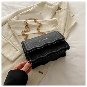 Detail of black pebbled leather crossbody bag with gold chain and scalloped flap edge