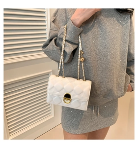 Detailed close-up of a white quilted shoulder bag with golden lock and chain strap