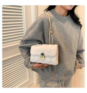 Detail of white quilted crossbody bag featuring a gold oval twist lock and chain strap